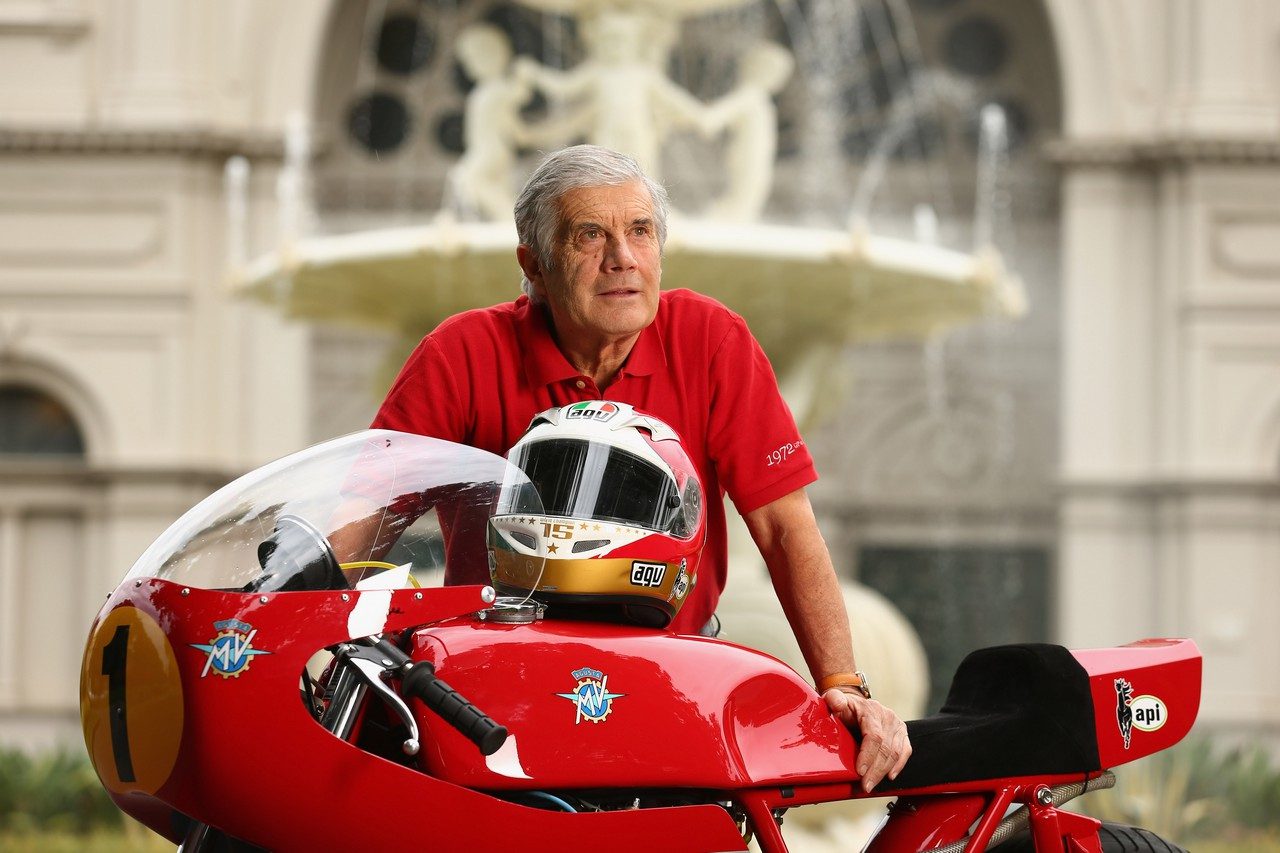 贾科莫·阿戈斯蒂尼(Giacomo Agostini)站在自行车旁，他在90年代中后期取得了许多成功