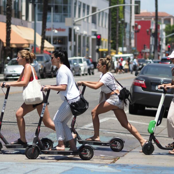 四名妇女穿过城市街道，背景中有几辆车骑着滑板车。