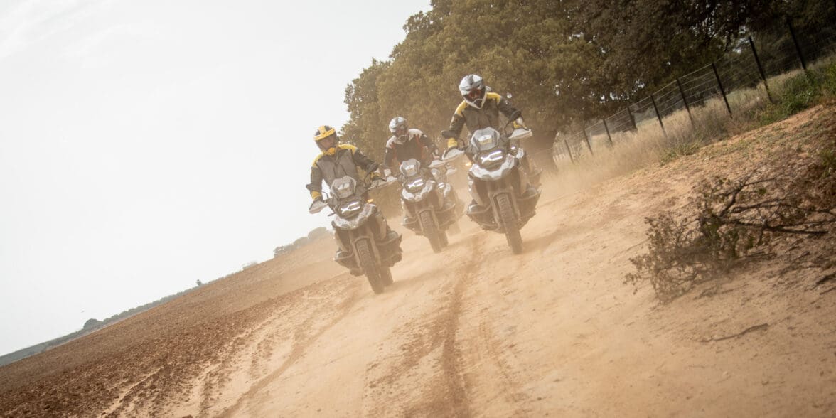 三个骑着宝马摩托车的人在一条土路上行驶的正面图像。