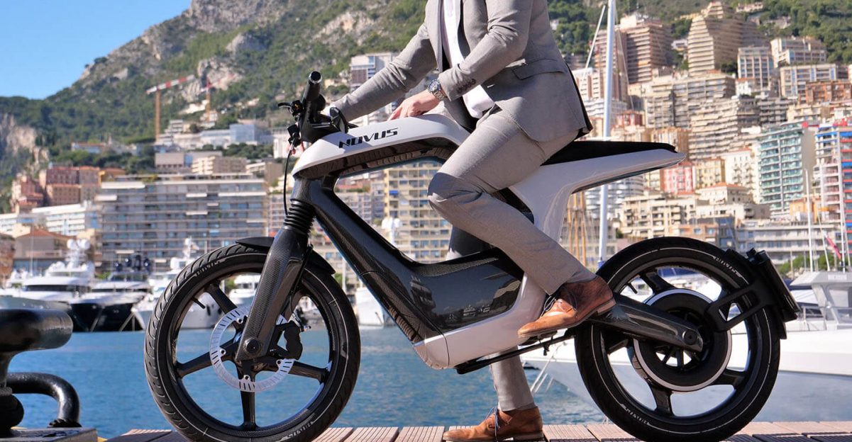 穿着棕褐色西装的模型，在码头上，尝试一辆Novus One Electric Motorcycle，带有湖泊在后台